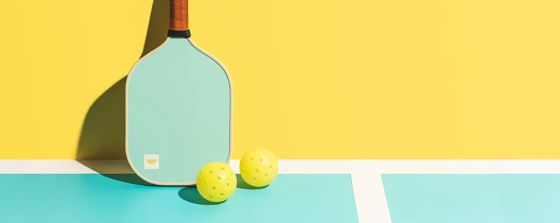 A pickleball paddle and ball on a yellow and green court.